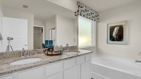 Primary bathroom with double sinks, white cabinets, granite countertops, and large bathtub.