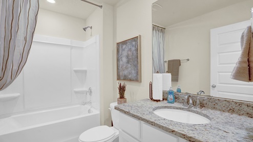 Second bathroom leading off the foyer with white cabinets, granite countertops, and combined shower and tub.