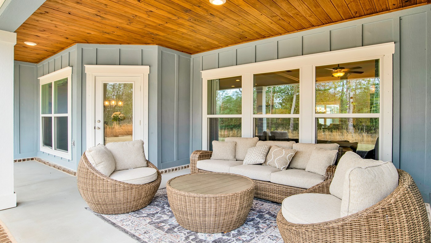 Covered back porch with seating areas by nice windows and treated wood under ceiling.