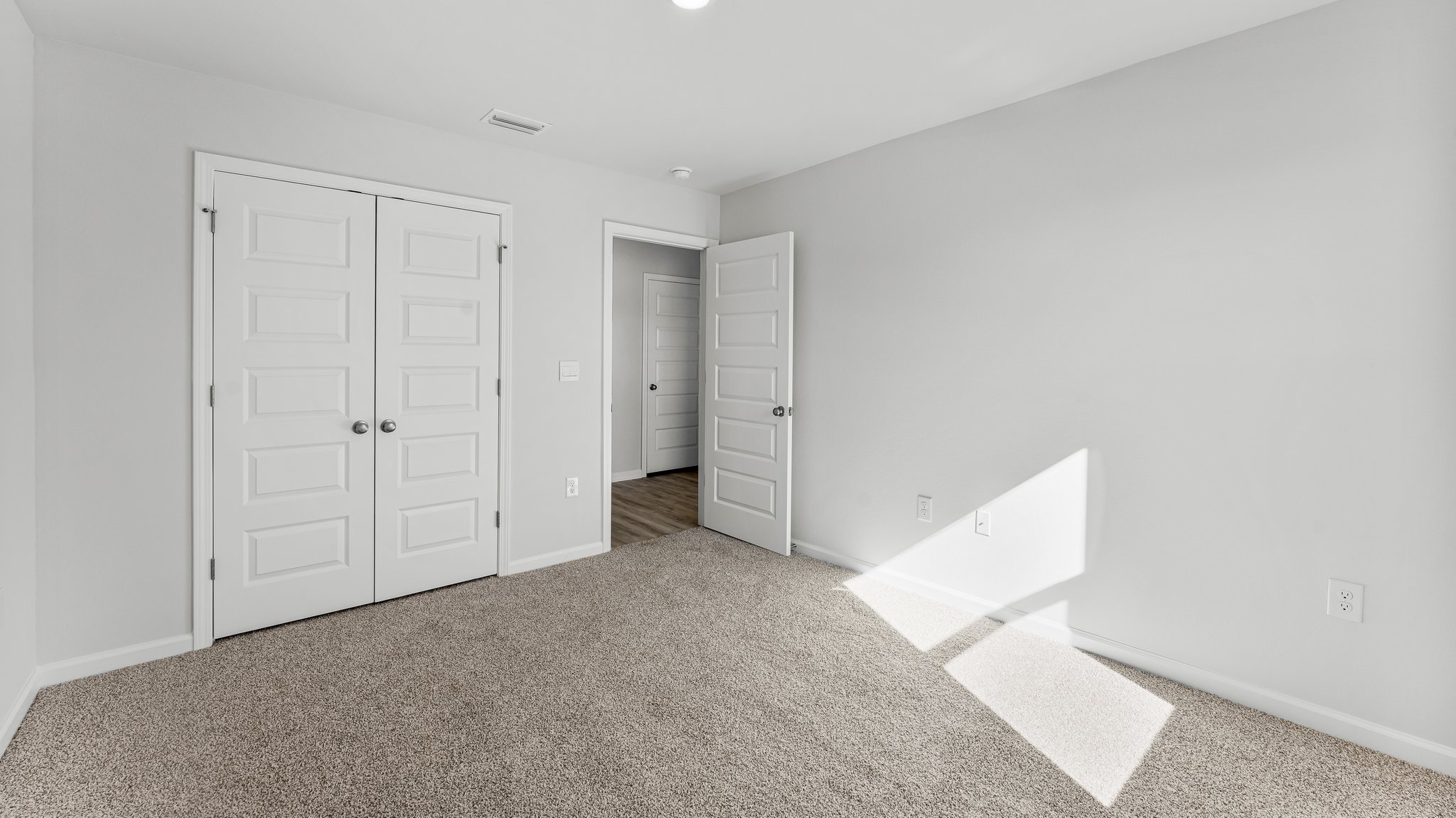 Spare bedroom with light-colored carpet.