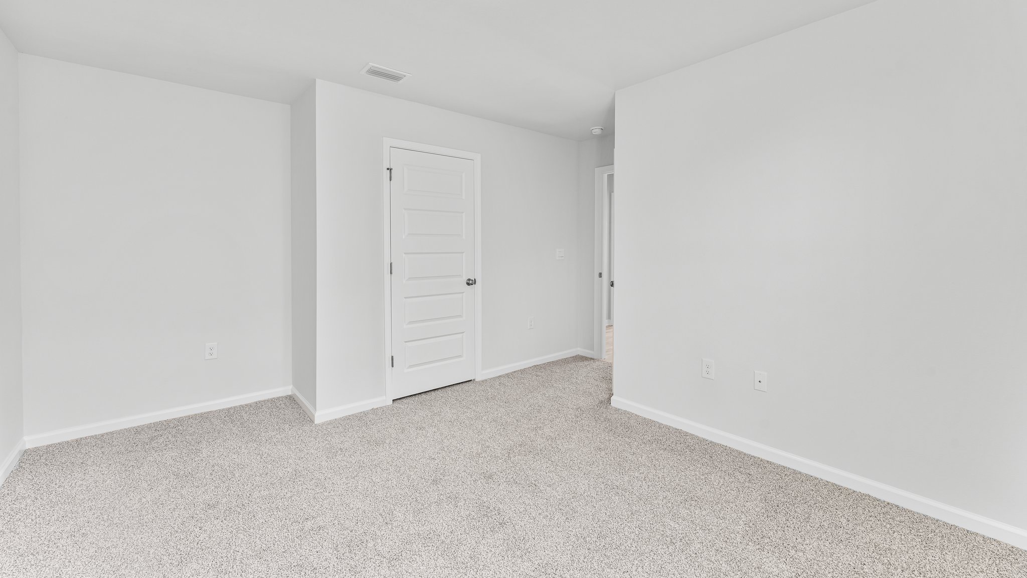 Spare bedroom with light-colored carpet.