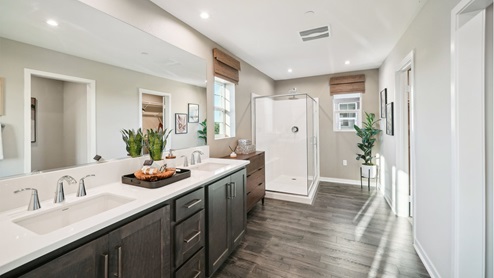 Spacious primary bathroom with dual sinks, brown cabinets, shower, laminate flooring