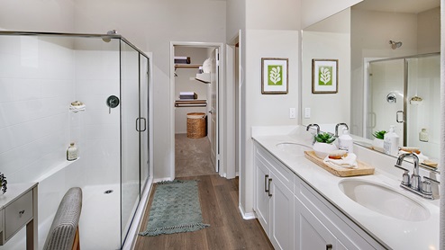 Primary bathroom with his and hers sink with white countertops and cabinets, walk-in shower, and closet