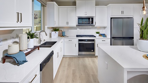 Vista Verde in Highland model home kitchen with white cabinets, stainless steel appliances, island with wood flooring