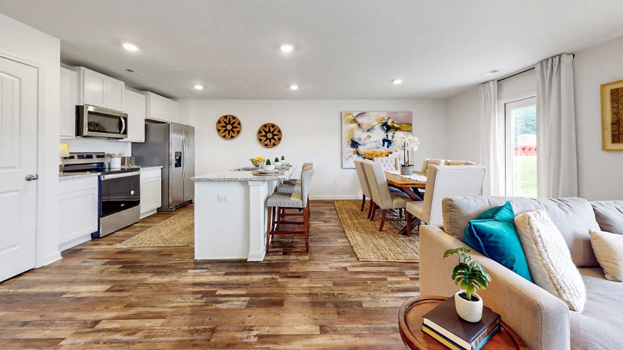 An open concept kitchen that opens to the dining room and the living room features an oversized kitchen island with 3 barstools, stainless steel appliances, white cabinets and a pantry