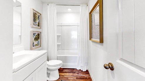 Burke – Bathroom 2 – A bathroom consisting of a tub/shower, toilet and vanity with white walls and wood floors, creating a clean and natural aesthetic