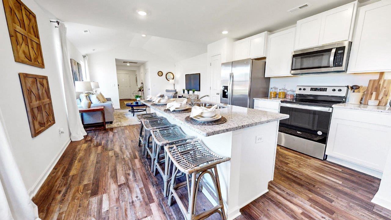 Kitchen with sleek stainless-steel appliances, a kitchen island with barstools and warm wooden floors.