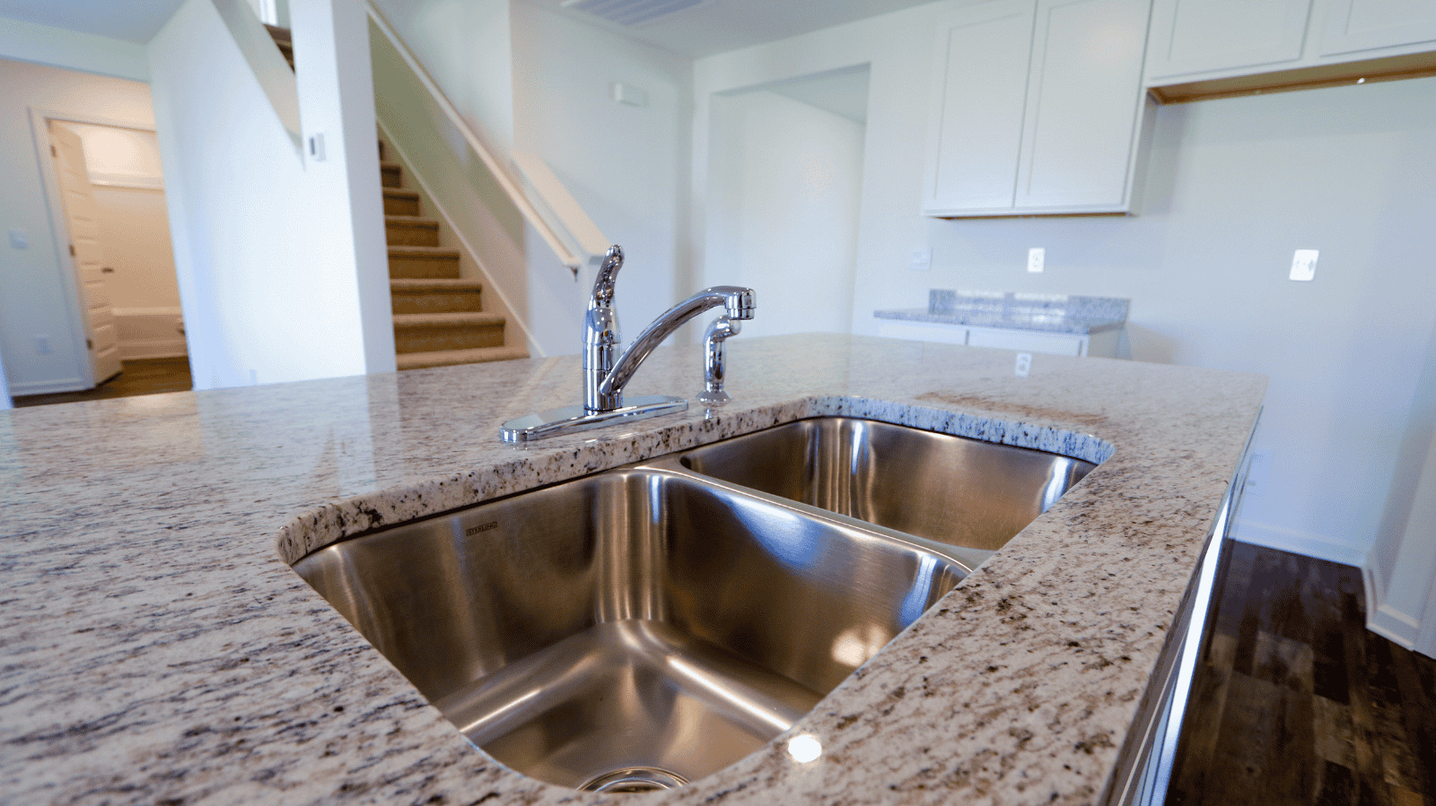 Stainless steel double sink with modern faucet installed in a granite countertop kitchen.