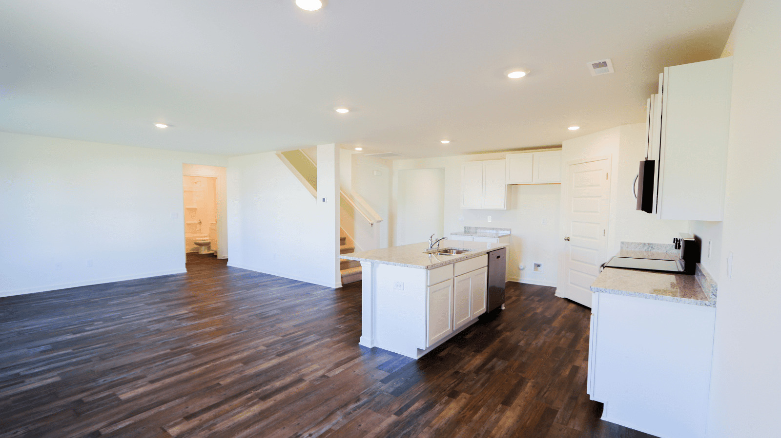 Open concept living area featuring a kitchen with white cabinetry, granite countertops, and hardwood floors.