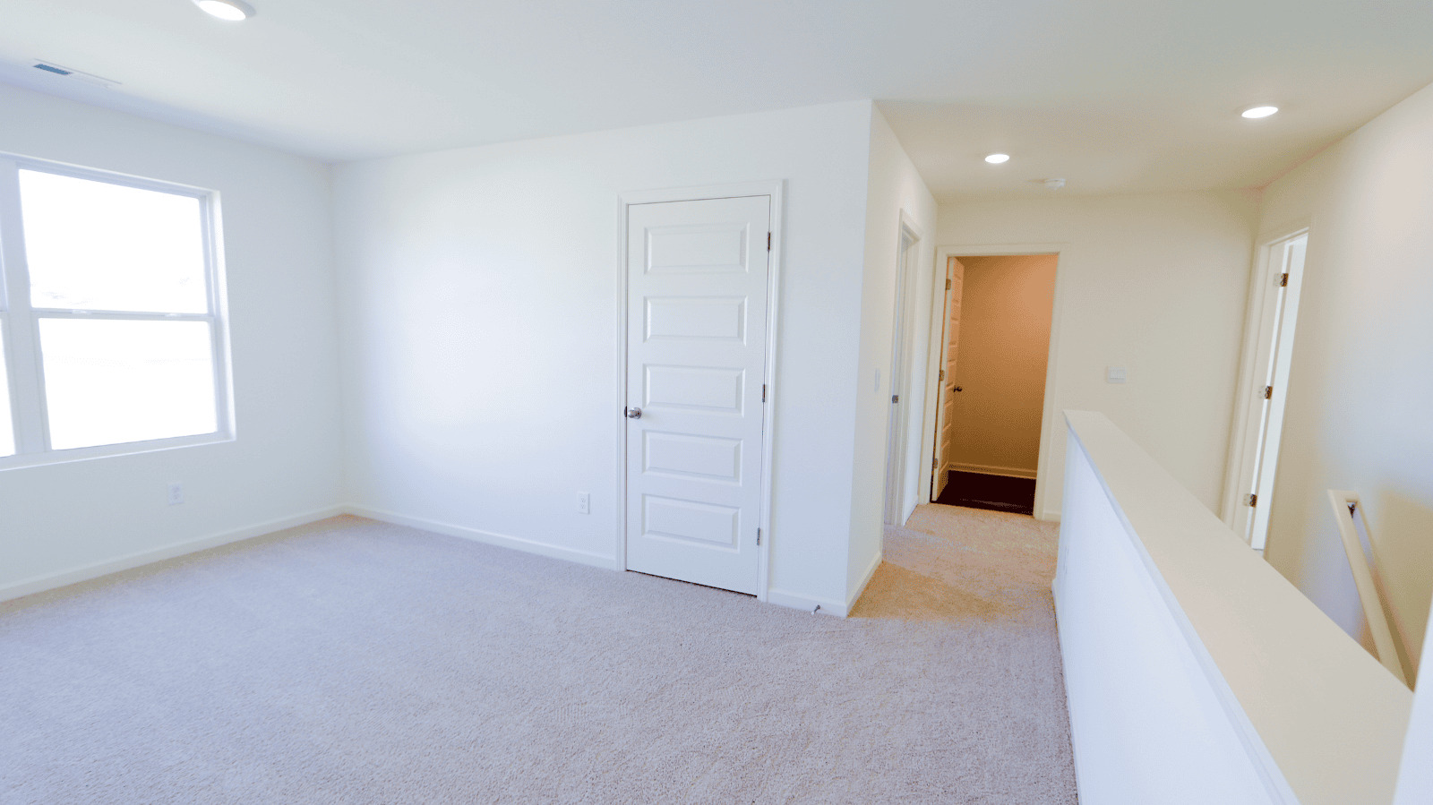 Bright and spacious hallway with carpet, leading to a room with large windows and white doors.