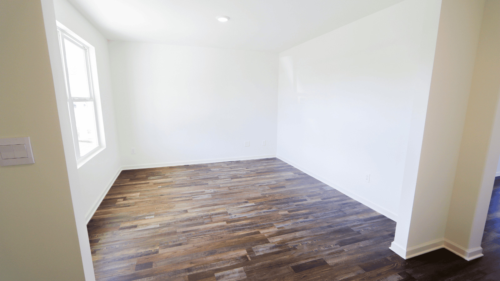 Bright, empty room with wood flooring and a large window, suitable for various interior design options.
