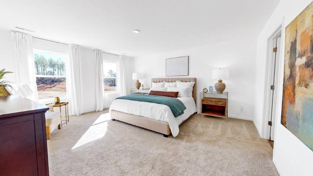 A very spacious bedroom featuring a king-sized bed, 2 nightstands, a dresser, a chair and side table and a door that leads to the primary bathroom