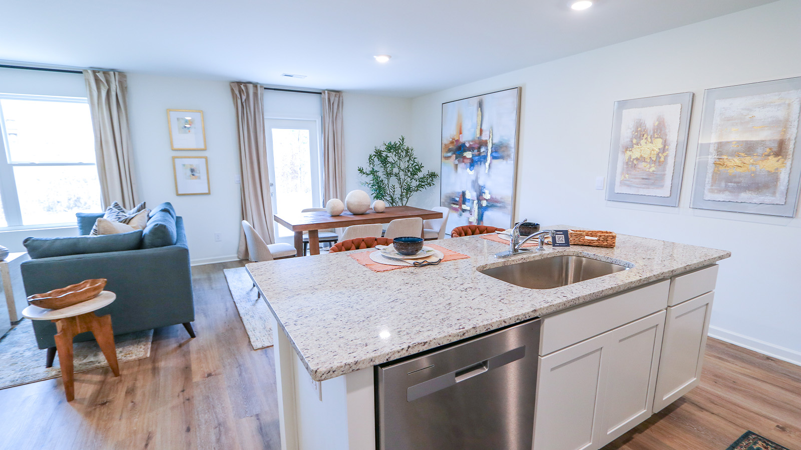 An open concept kitchen that opens to the dining room and the living room features an oversized kitchen island with 3 barstools, stainless steel appliances, white cabinets and a pantry.