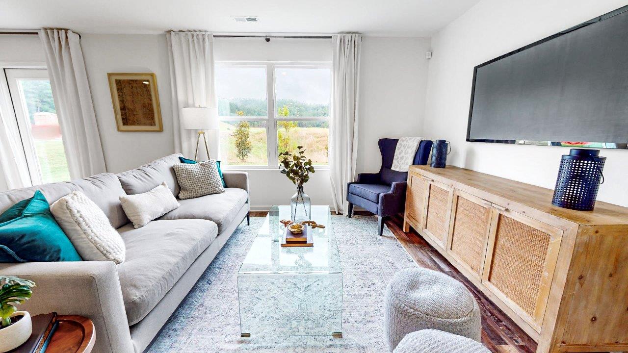 Spacious living room that features a couch, two poofs, a coffee table, a media consol and an accent chair