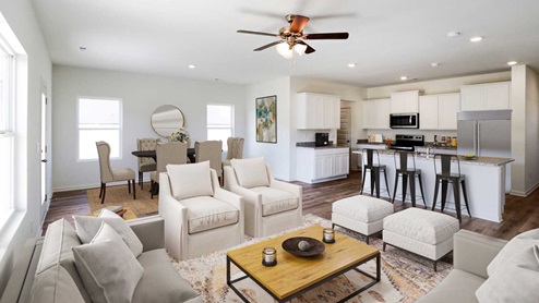 n open living area with light wood flooring, neutral-colored walls, and a ceiling fan with lights in the center of the room. The space is bright and airy, with natural light streaming in from large windows on one side. Multiple doors lead to other rooms, contributing to the open-concept layout that connects the living area seamlessly with the kitchen.