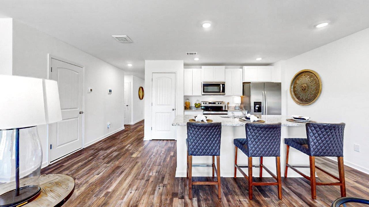 Open concept kitchen that opens to the dining room and the living room features an oversized kitchen island with 3 barstools, stainless steel appliances, white cabinets and a pantry
