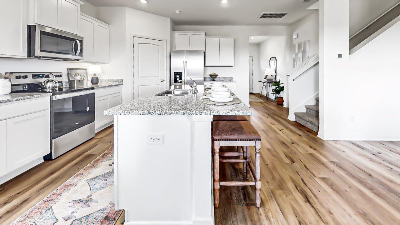 A view of the expansive kitchen that includes stainless steel appliances, white cabinets, a large island, a walk in pantry and the stairs that lead you to the upstairs