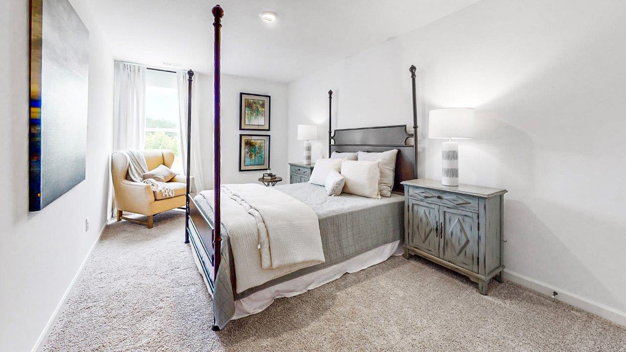 The second bedroom is shown here staged with a queen sized bed, two nightstands, and an armchair.