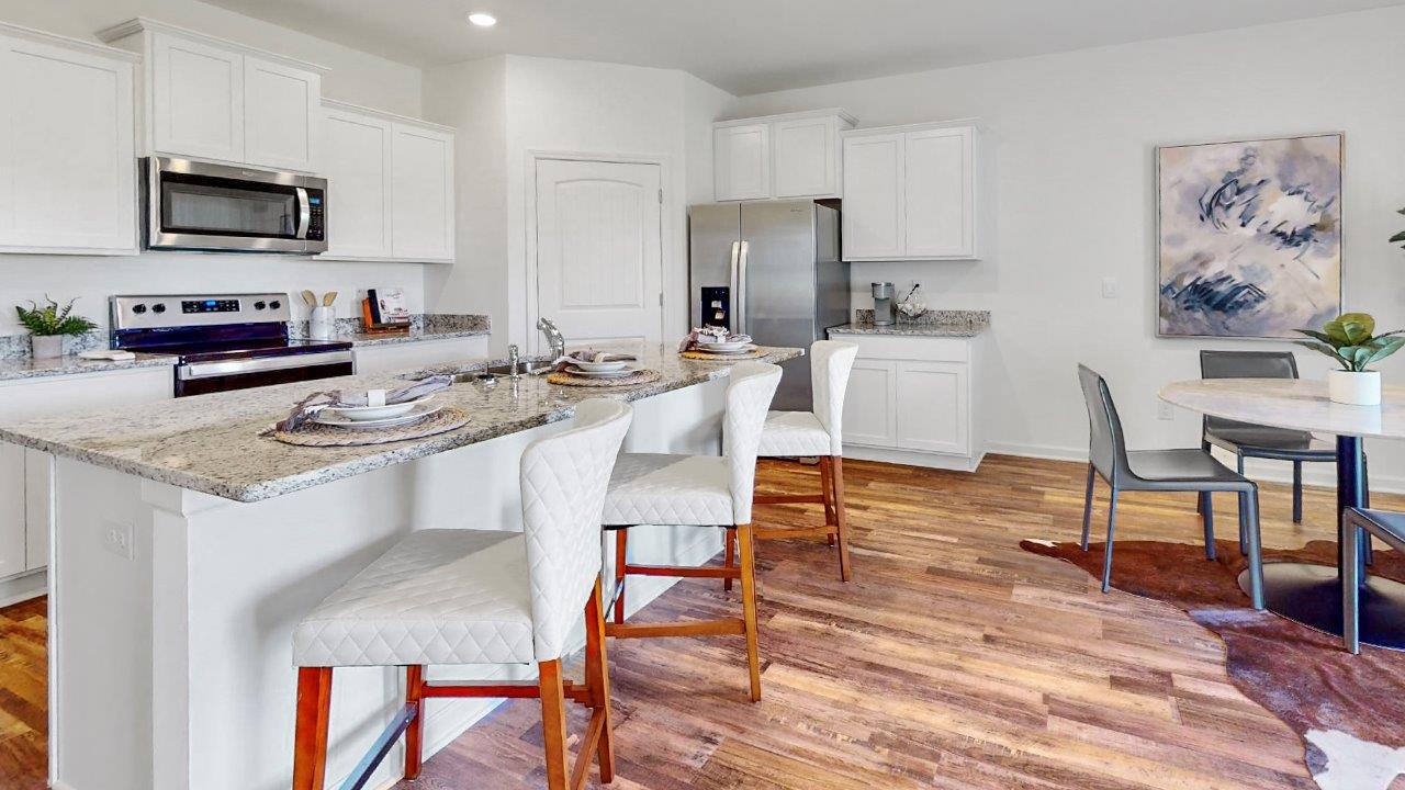 A large kitchen with an oversized island and barstools, equipped with stainless steel appliances and a walk in corner pantry