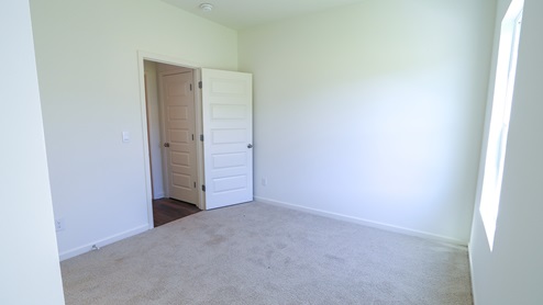 The downstairs bedroom has a large window allowing natural light to stream throughout the carpeted space.