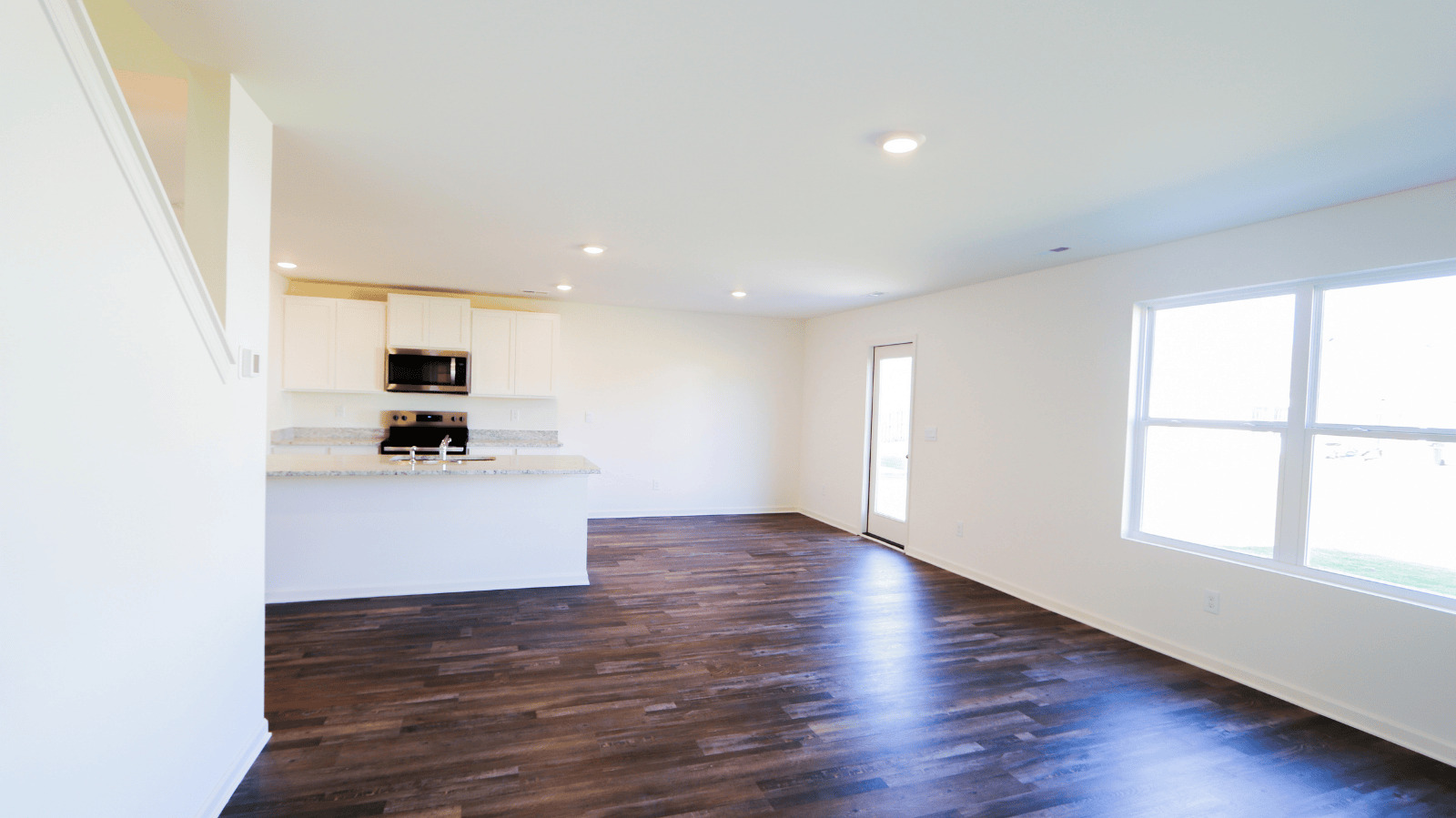 Open concept living area featuring a kitchen with white cabinetry, granite countertops, and hardwood floors.