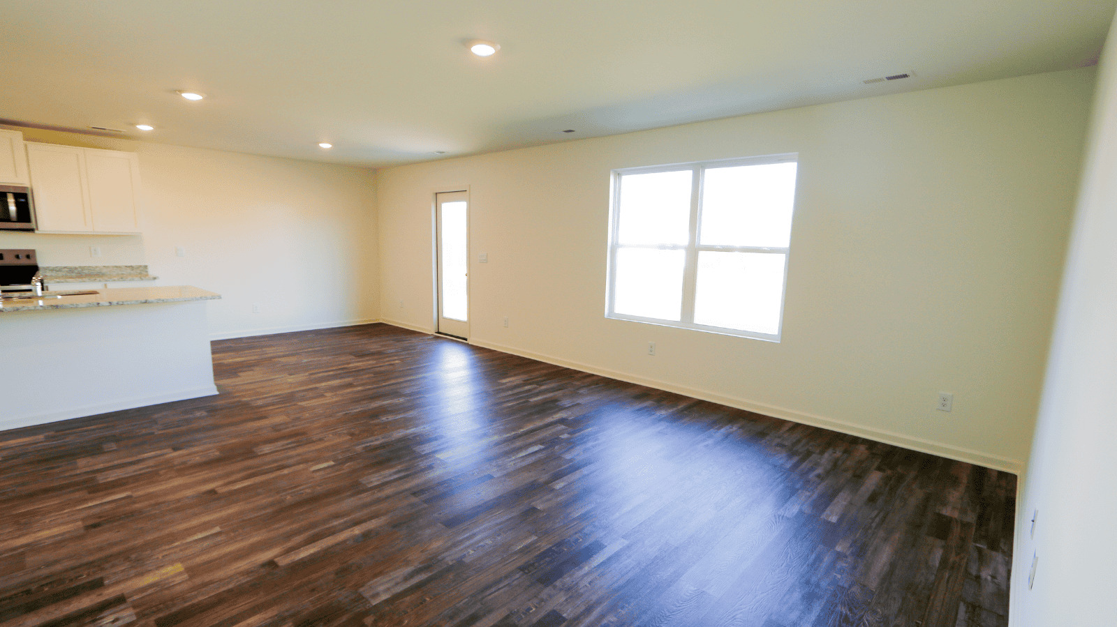 Bright open living space with kitchen area, featuring hardwood floors and large windows for natural light.