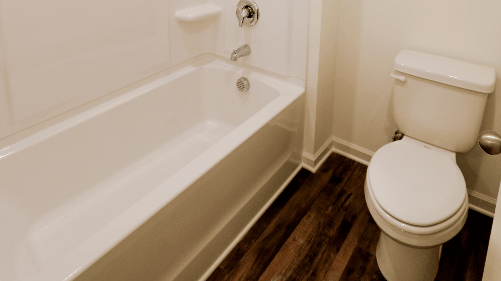 Modern bathroom featuring a white bathtub, toilet, and wood-like flooring.