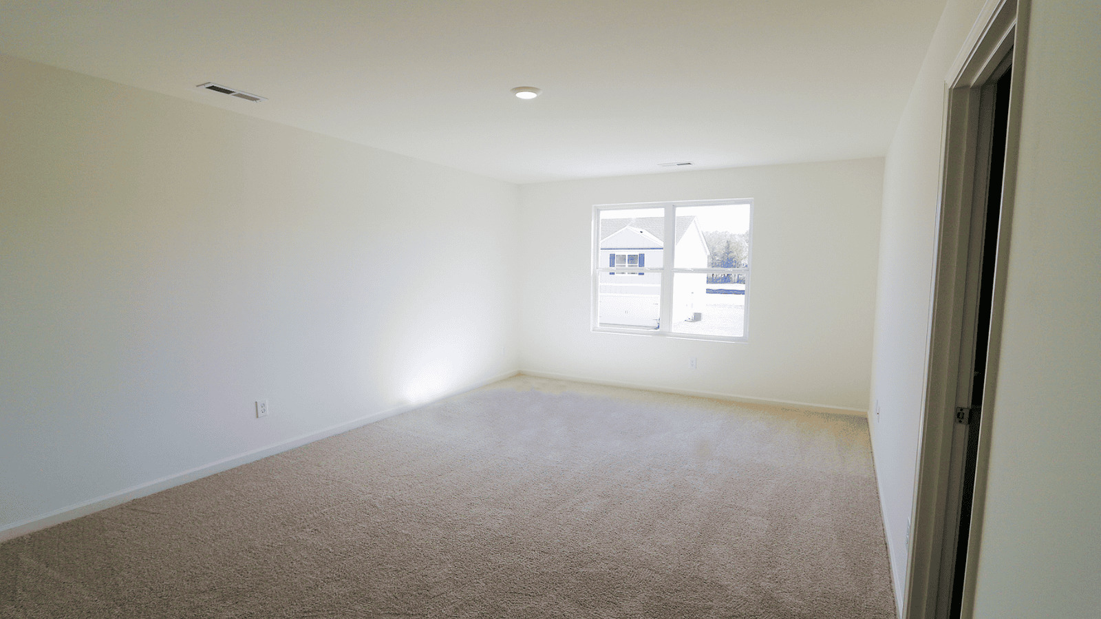 Spacious empty room with beige carpet and large window, providing natural light and a view of the outside.