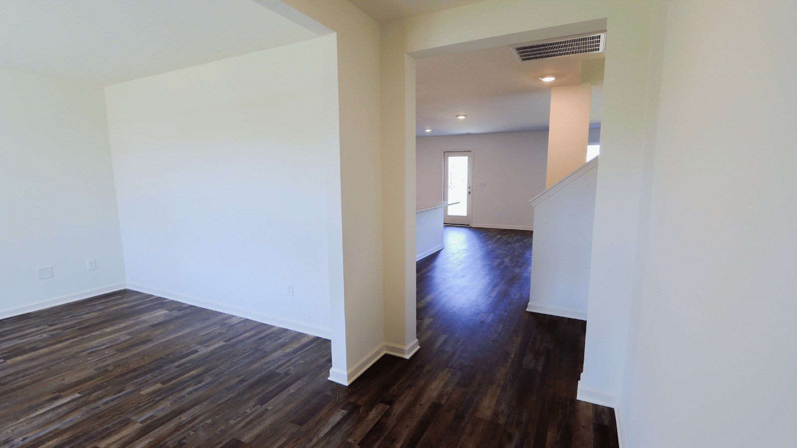 Open living space with dark wood floors, leading to a bright entrance and staircase in a new house layout.
