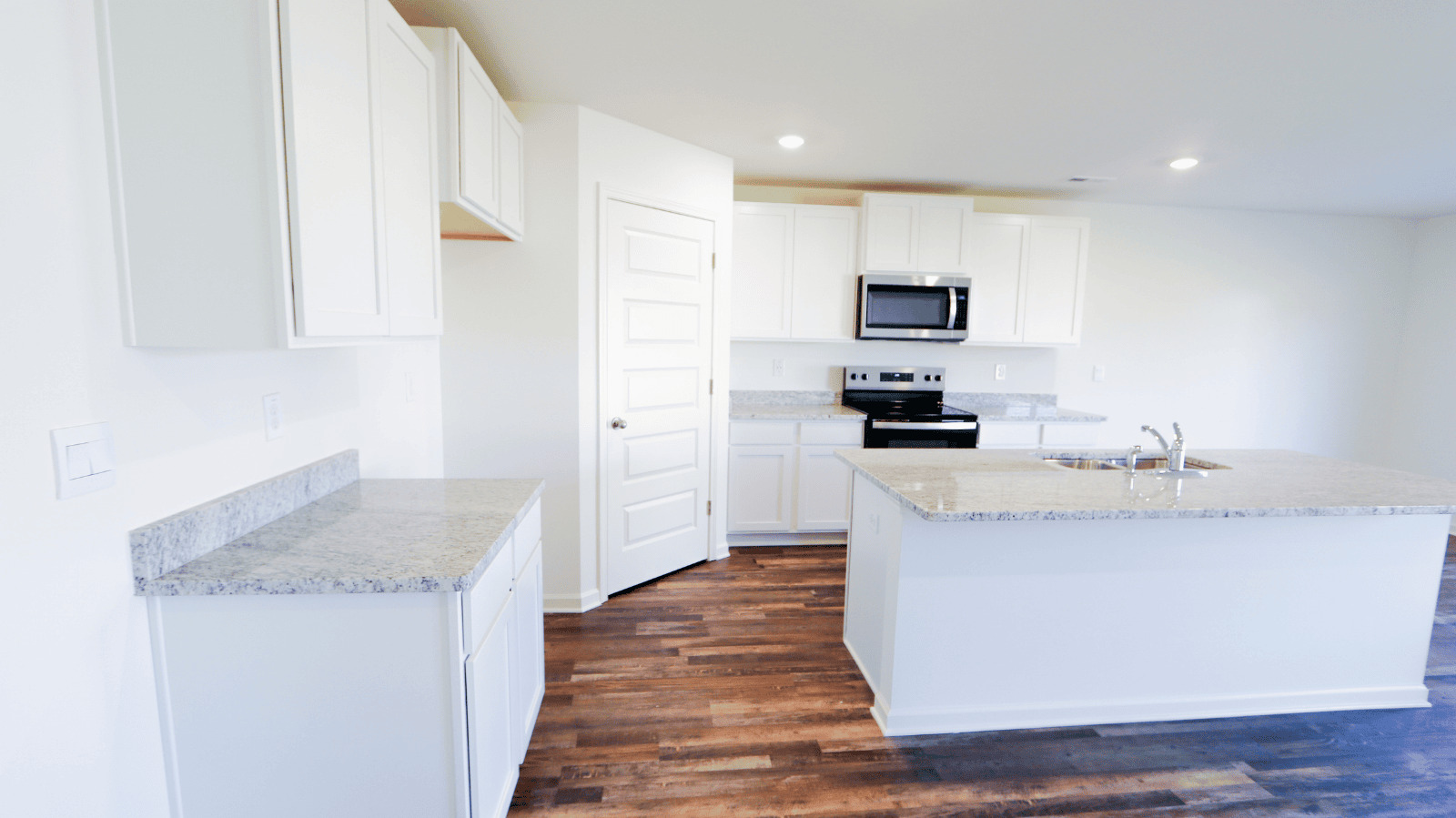 Modern kitchen featuring white cabinetry, a stainless-steel microwave, and a large island with granite countertops.