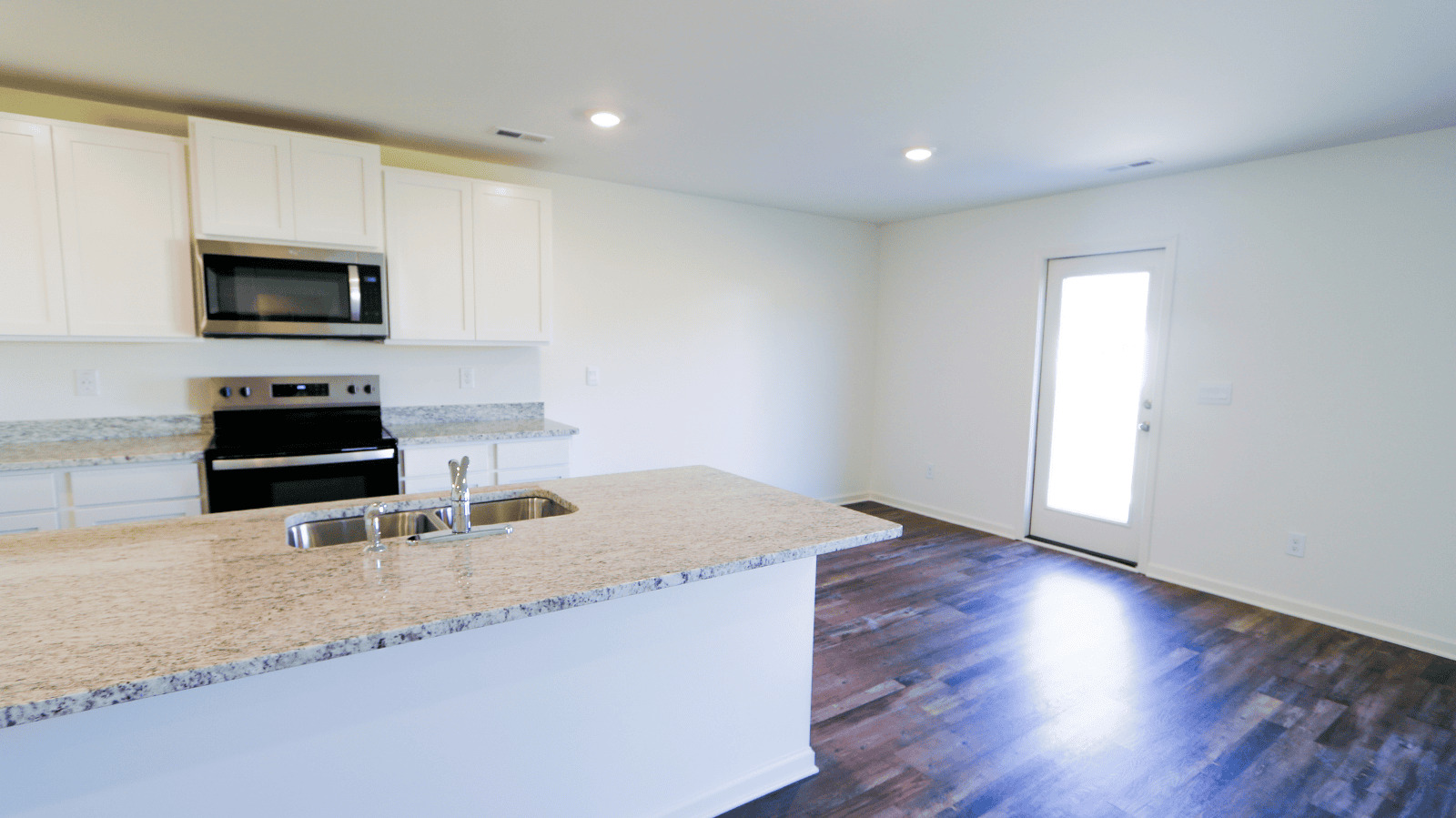 Modern kitchen with granite countertops, stainless steel appliances, and open layout leading to living area and entrance door.