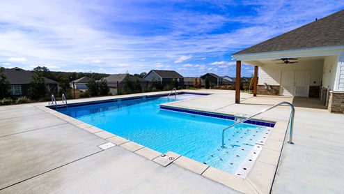 A serene outdoor pool area featuring clear blue water, surrounded by houses and under a bright blue sky.