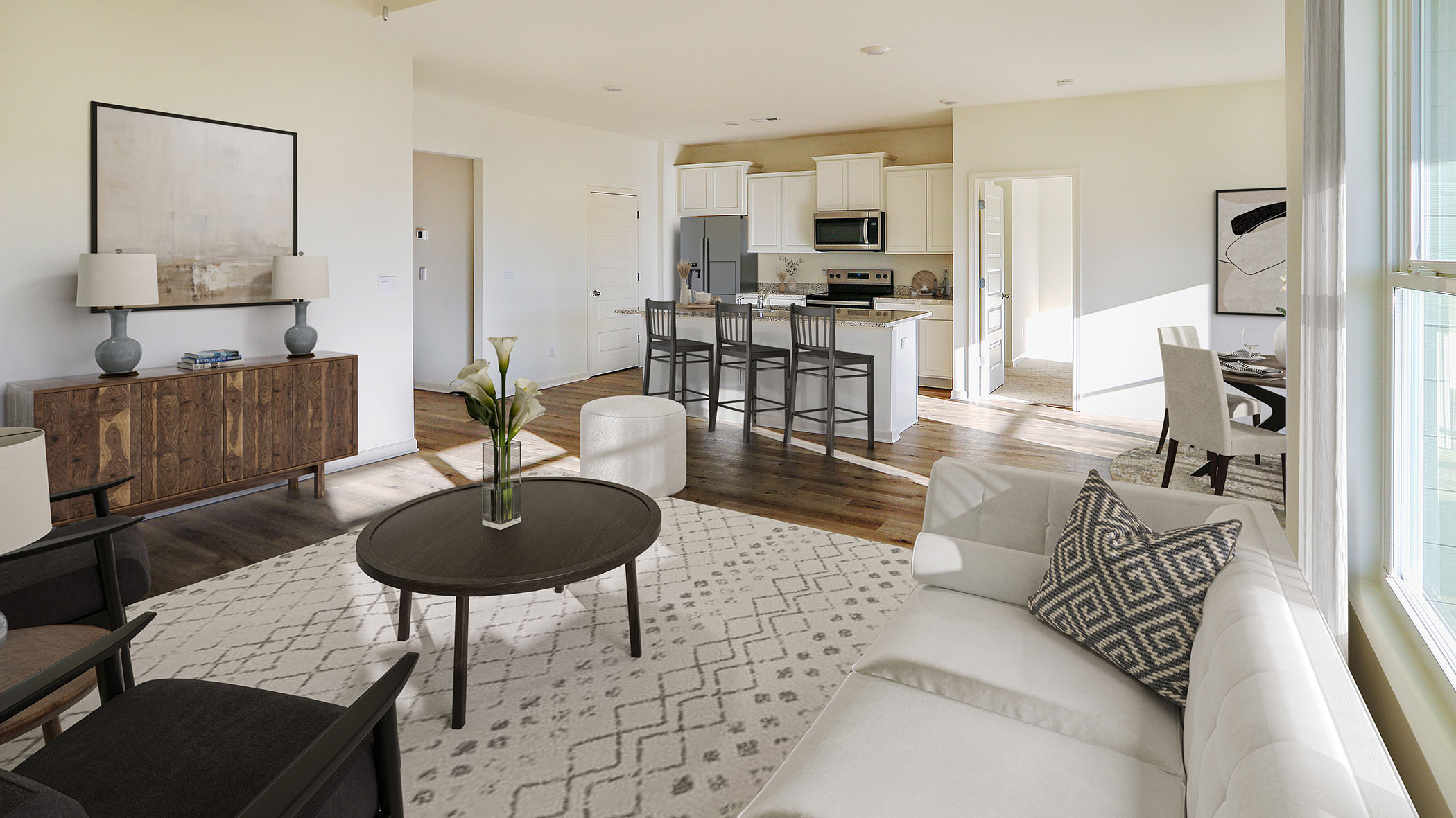 Modern open-concept living room and kitchen with stylish furnishings, hardwood floors, and natural light. Features a comfortable white sofa with a patterned pillow, a large area rug, and a wooden cabinet. Perfect for contemporary home interiors and design inspiration.