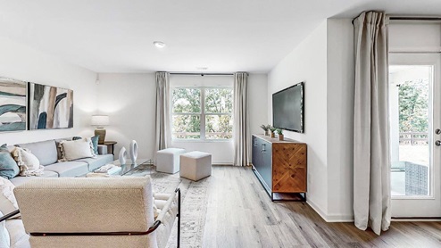 Bright open living room with a couch, 2 chairs, 2 poofs and amedia consol with flat screen television