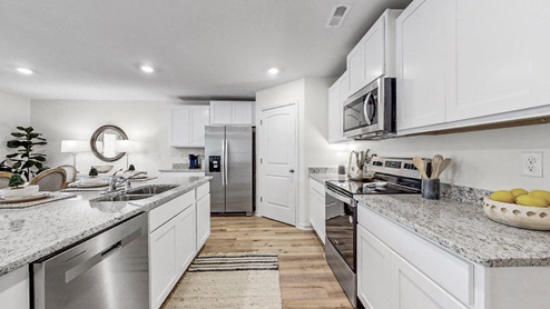 a different view of the kitchen that shows the white kitchen cabinets, as well as stainless steel appliances and the walk in pantry