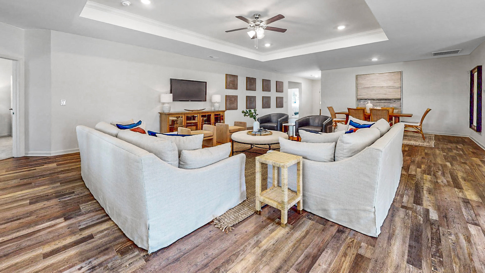 Contemporary dining room with a wooden table and six wicker chairs, featuring a large abstract painting and decorative white vases, set on a patterned rug, complemented by light walls and floor-to-ceiling mirror, showcasing modern interior design.