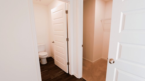 Interior view of bathroom doorway with a toilet visible and an adjacent closet featuring a wire shelf.