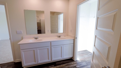Modern bathroom featuring a double vanity with mirrors, light-colored walls, and a doorway leading to a closet space.