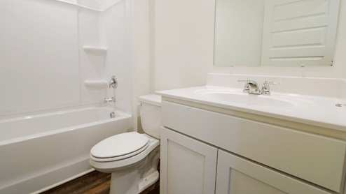 Modern bathroom with a bathtub, toilet, and white cabinetry, featuring neutral tones and ample natural light.
