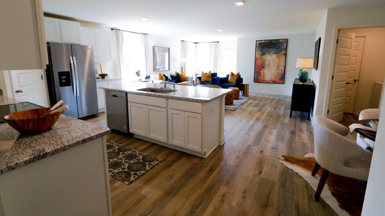 A view of the open concept kitchen and living room, shown here staged with a full suite of living room furniture and a full dining table and chairs.