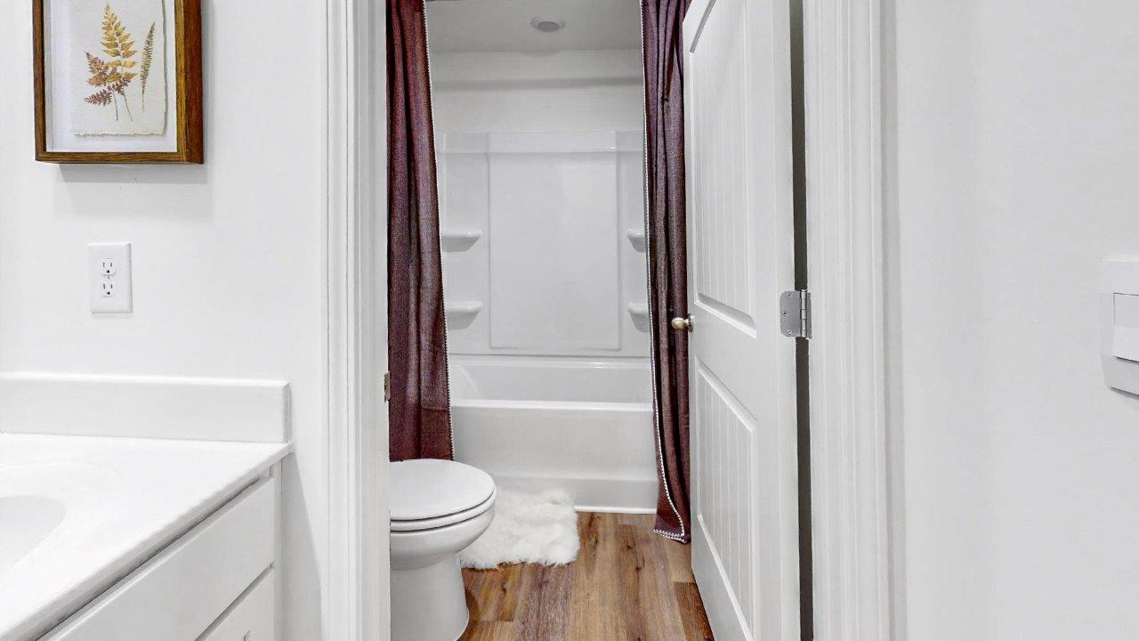 A bathroom featuring a white sink, toilet, and shower, with a door providing separation from the adjacent room.