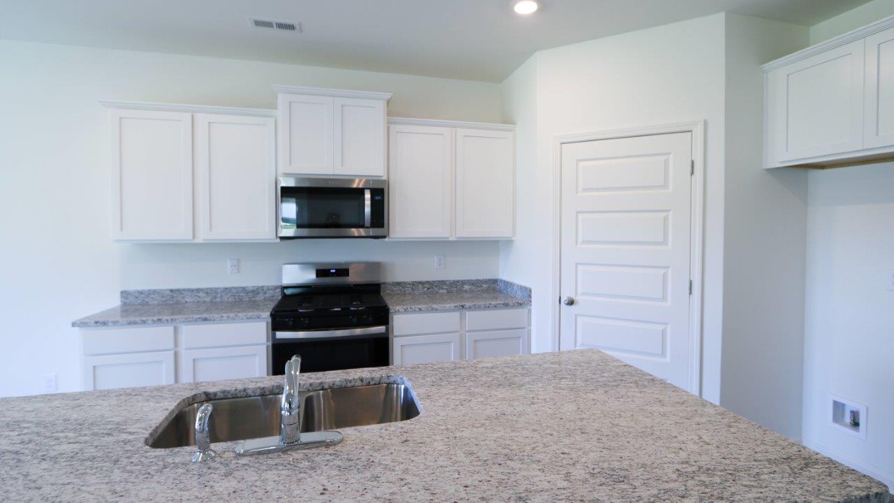 Modern kitchen interior with white cabinets, granite countertops, and stainless-steel appliances.