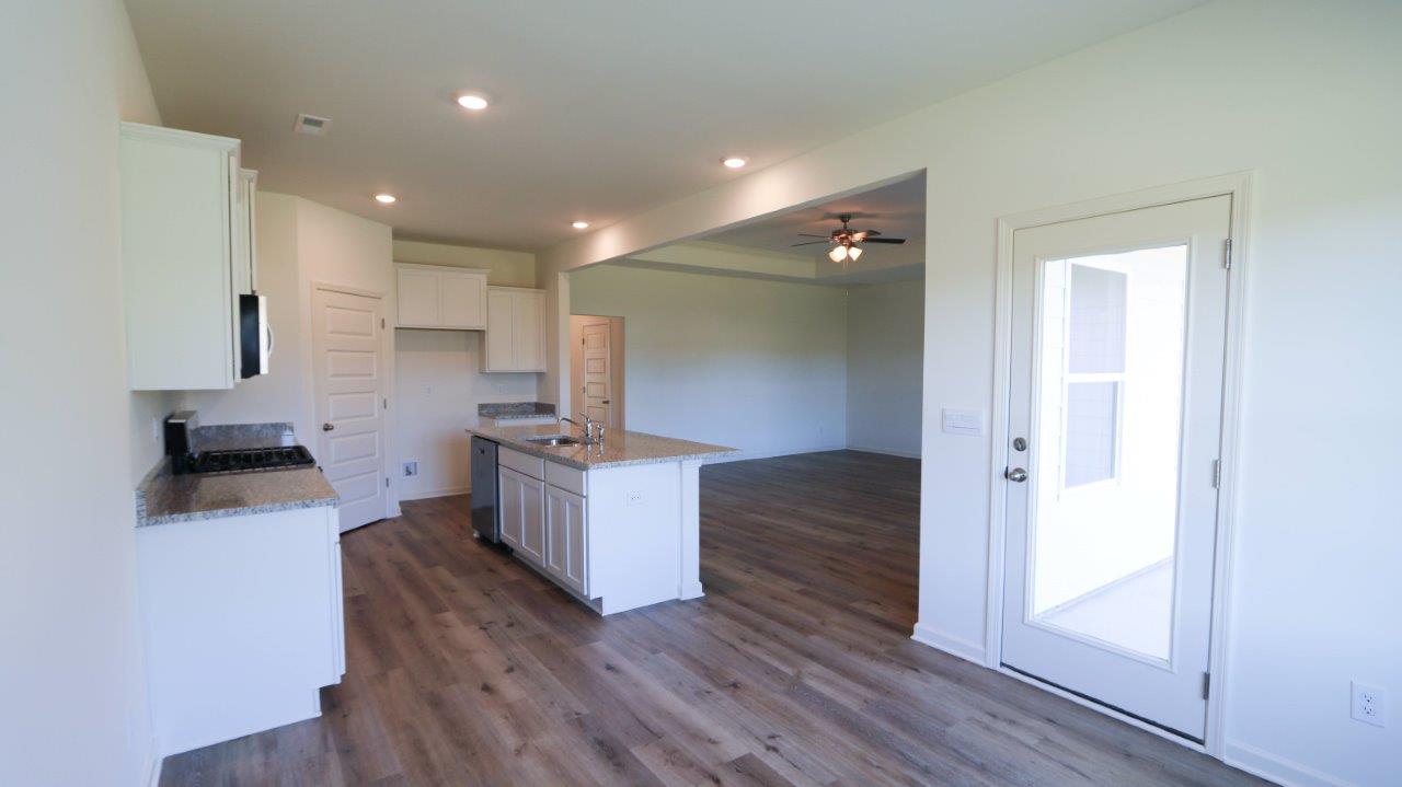 Modern empty kitchen with white cabinets, granite countertops, and wood flooring, leading to a living area.
