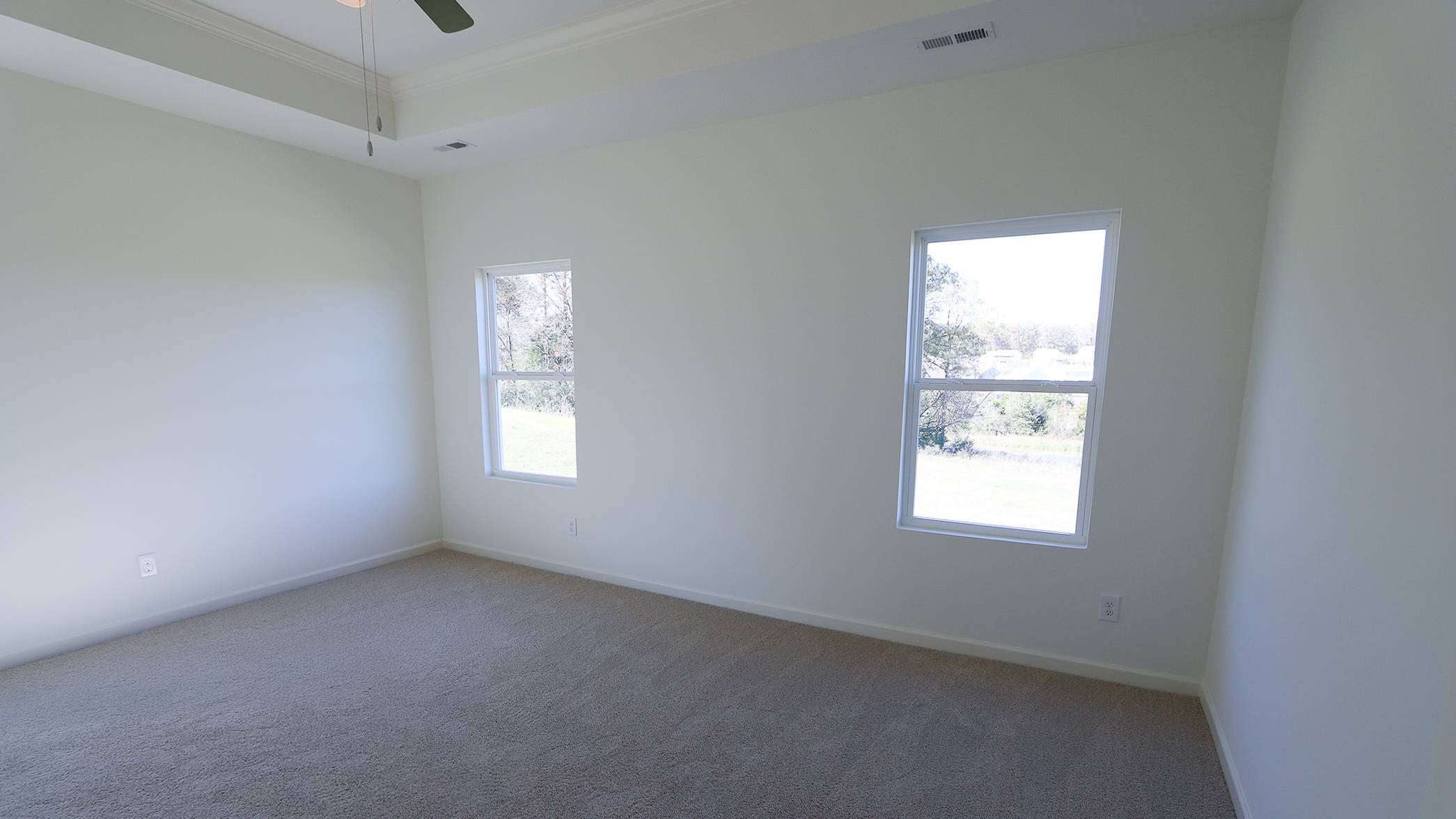 Empty room with beige carpet, white walls, two windows, and a ceiling fan.