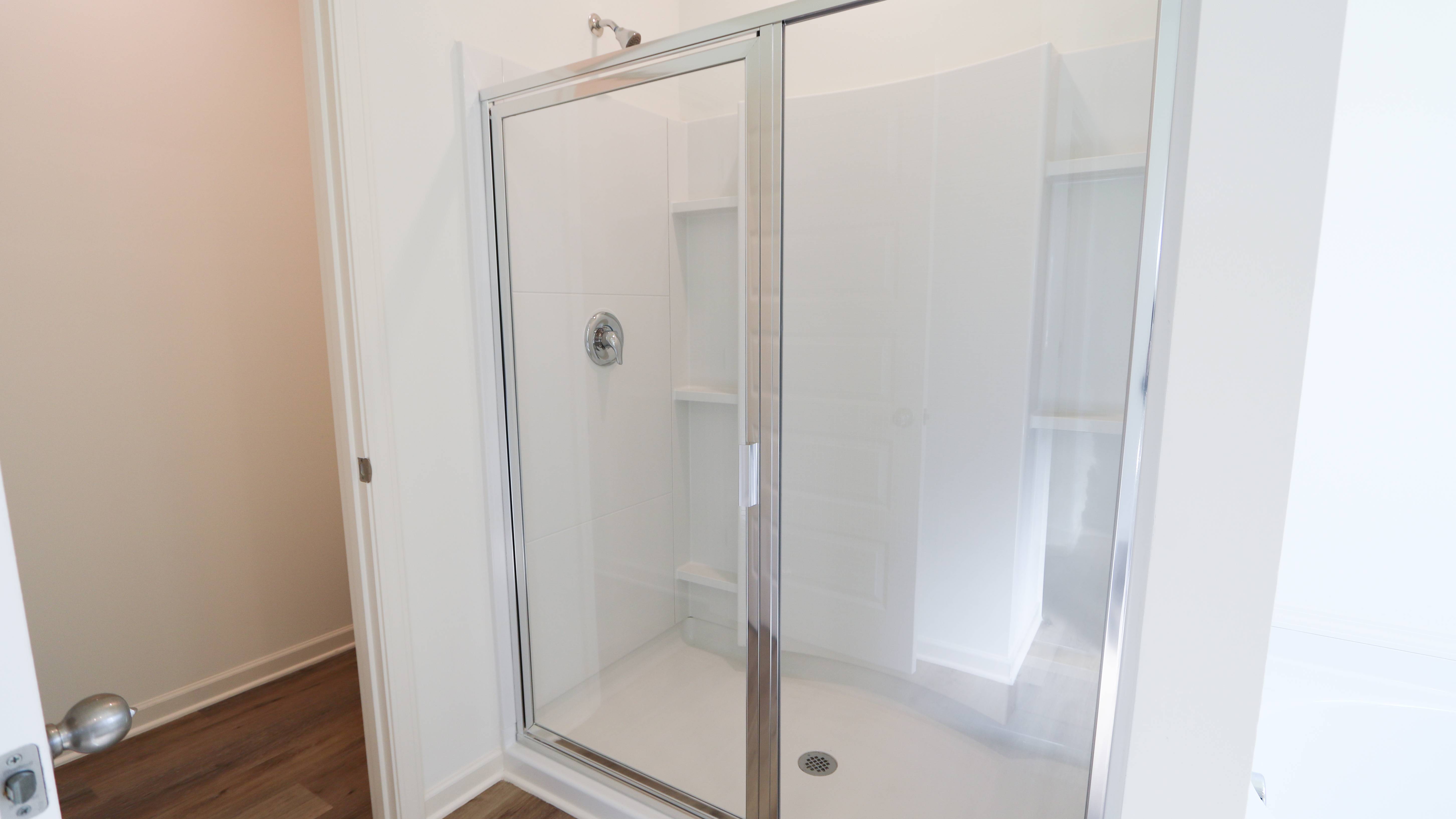 Modern corner shower with glass doors in a clean, white bathroom.