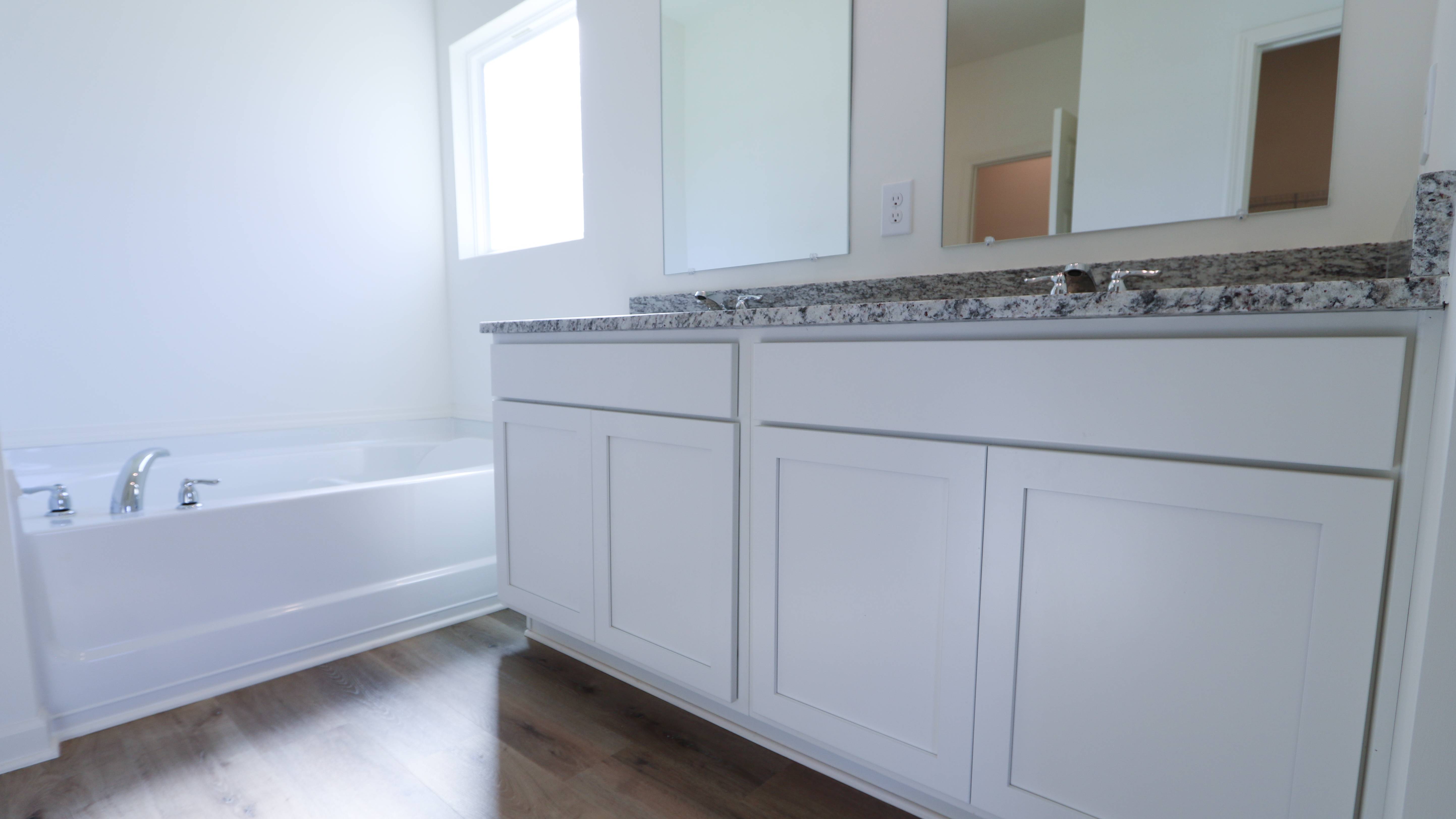 Modern bathroom with white cabinets, granite countertop, and a bathtub.