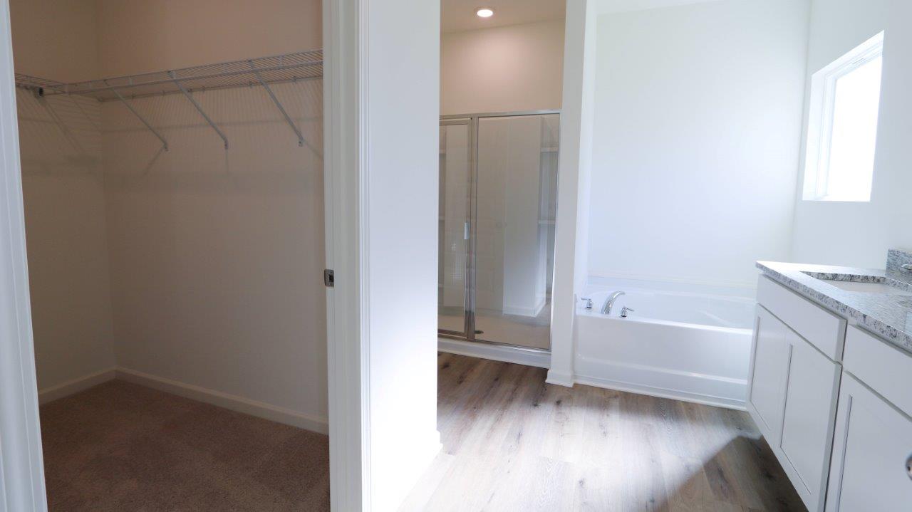 A neat, empty closet on the left and a clean bathroom with a tub, shower, and vanity on the right.