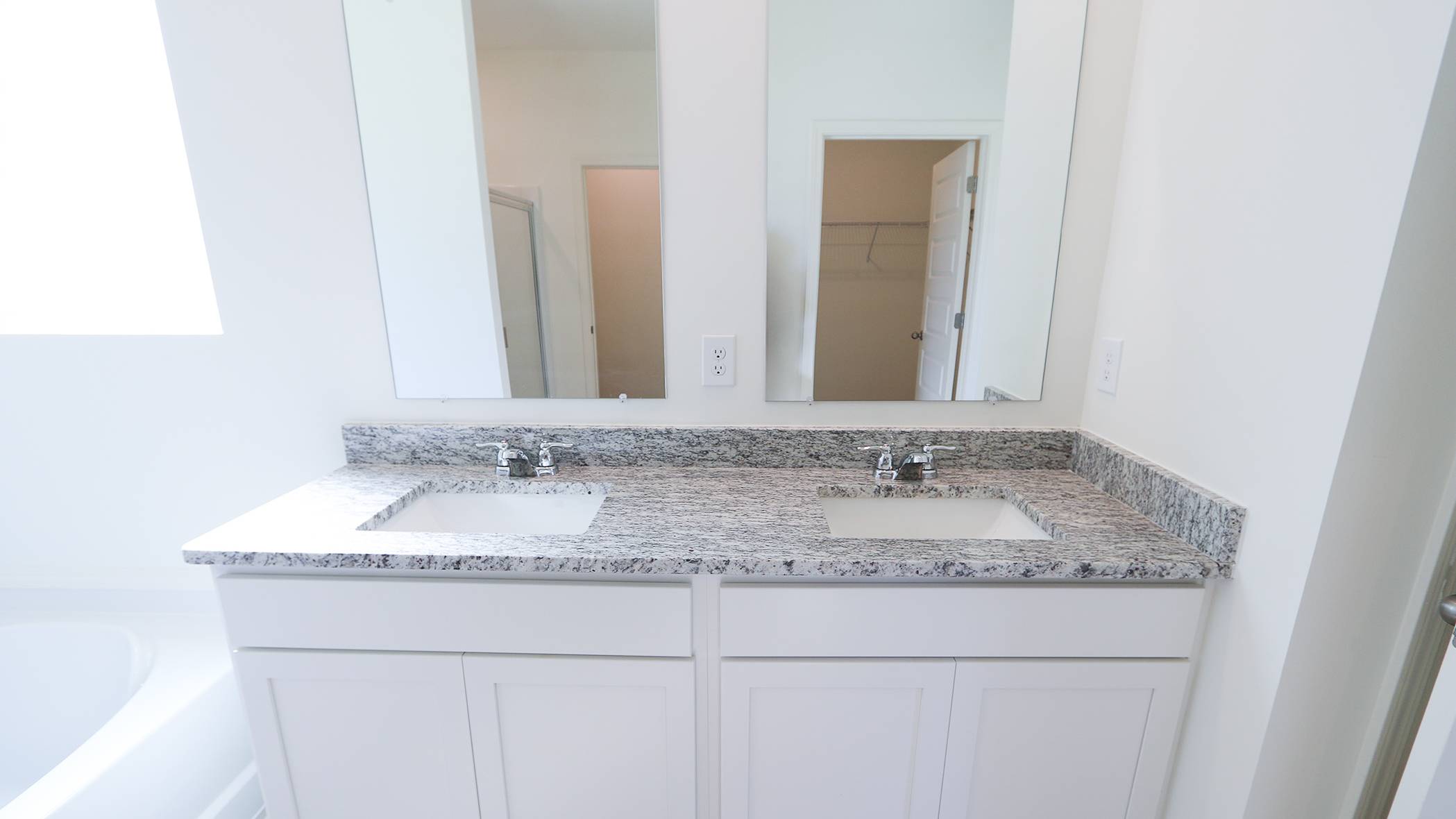 Modern bathroom with a white double vanity and granite countertop, large mirror, and neutral tones.