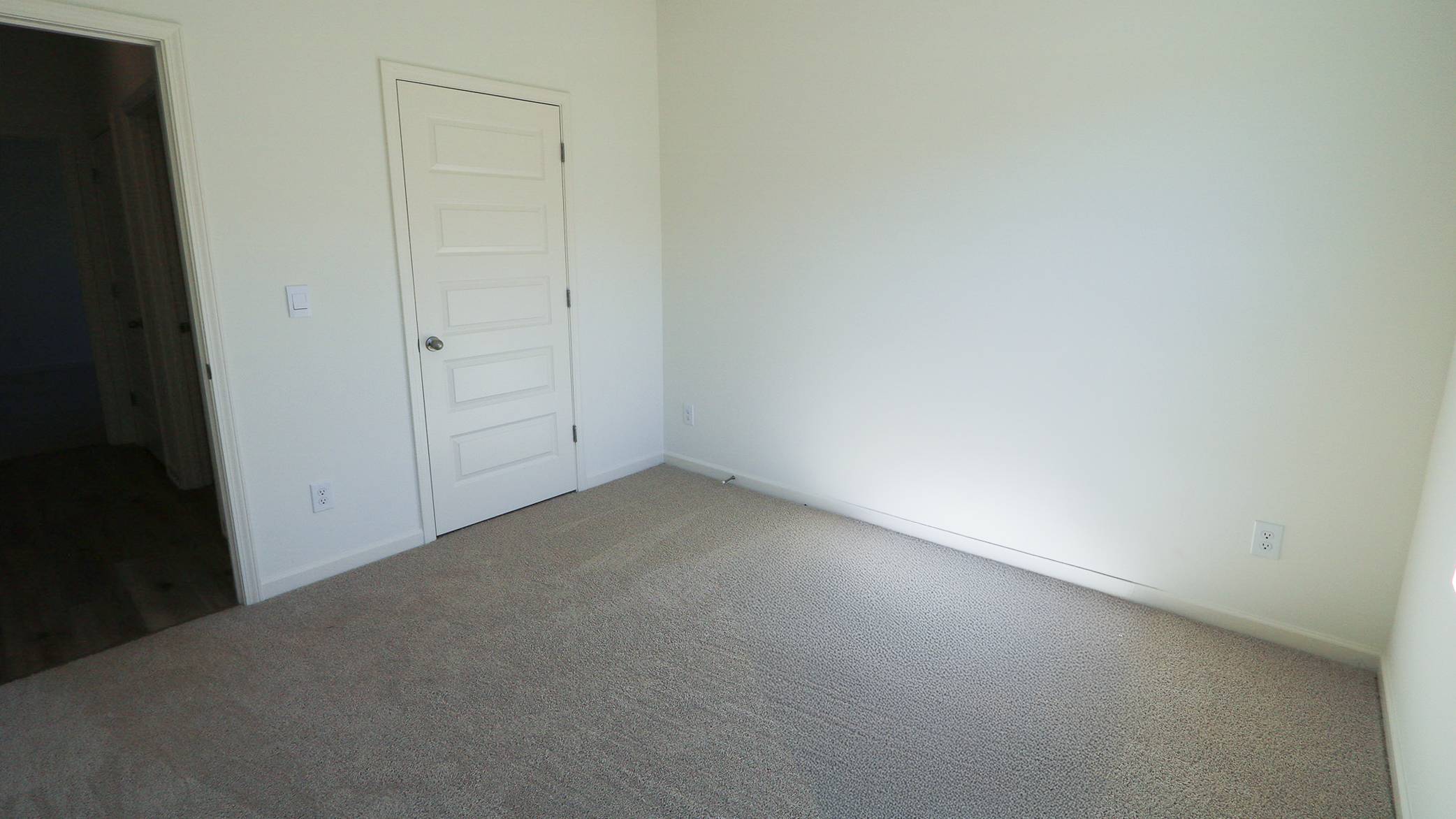 Empty room with beige carpet, white walls, and a closed door.