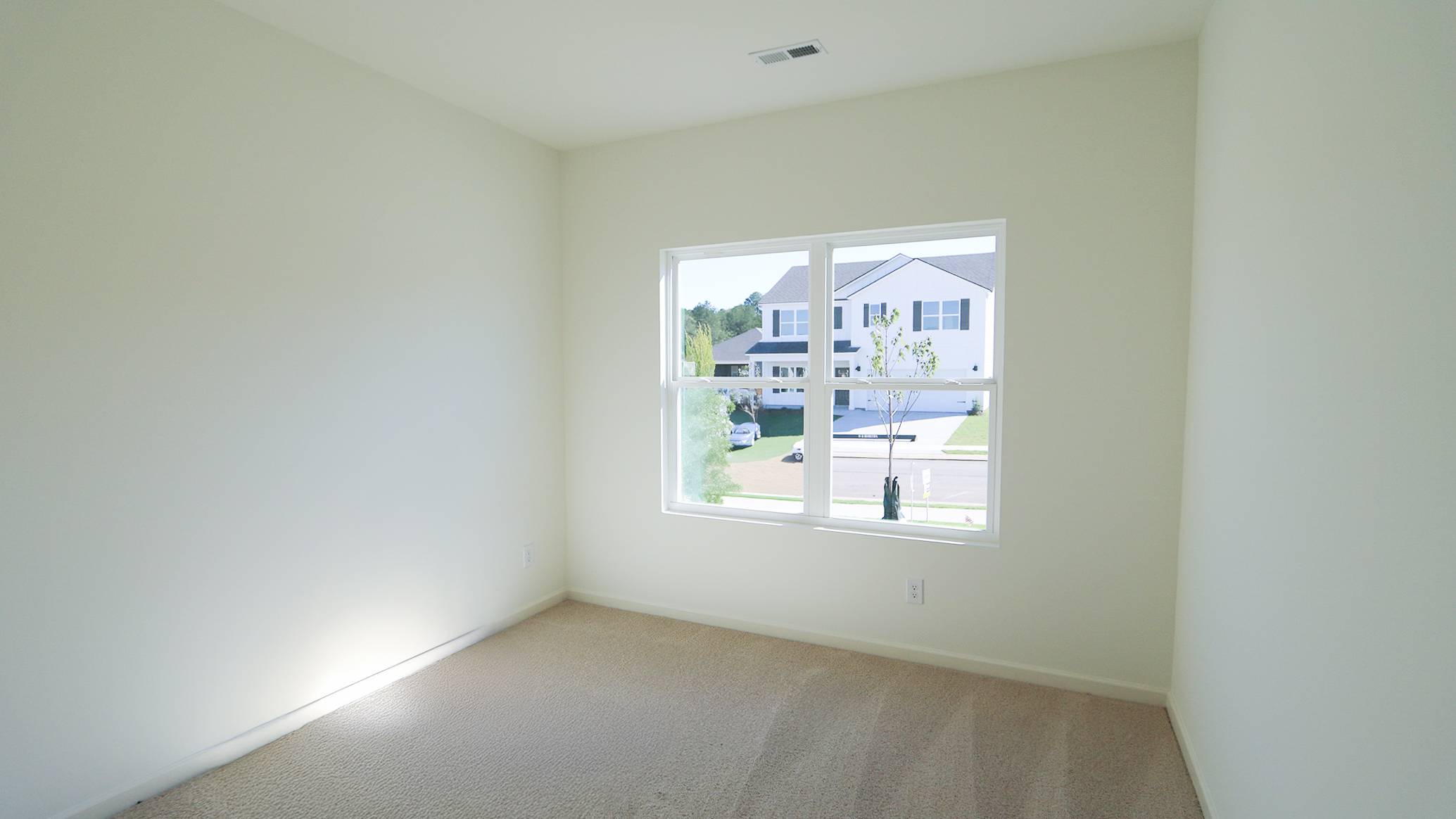 Empty room with carpet, a window showing houses, and a clear blue sky.